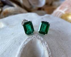 Pair of rectangular emerald-green stone stud earrings displayed on white fabric.+