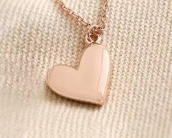 Rose gold heart pendant necklace displayed on soft beige fabric.